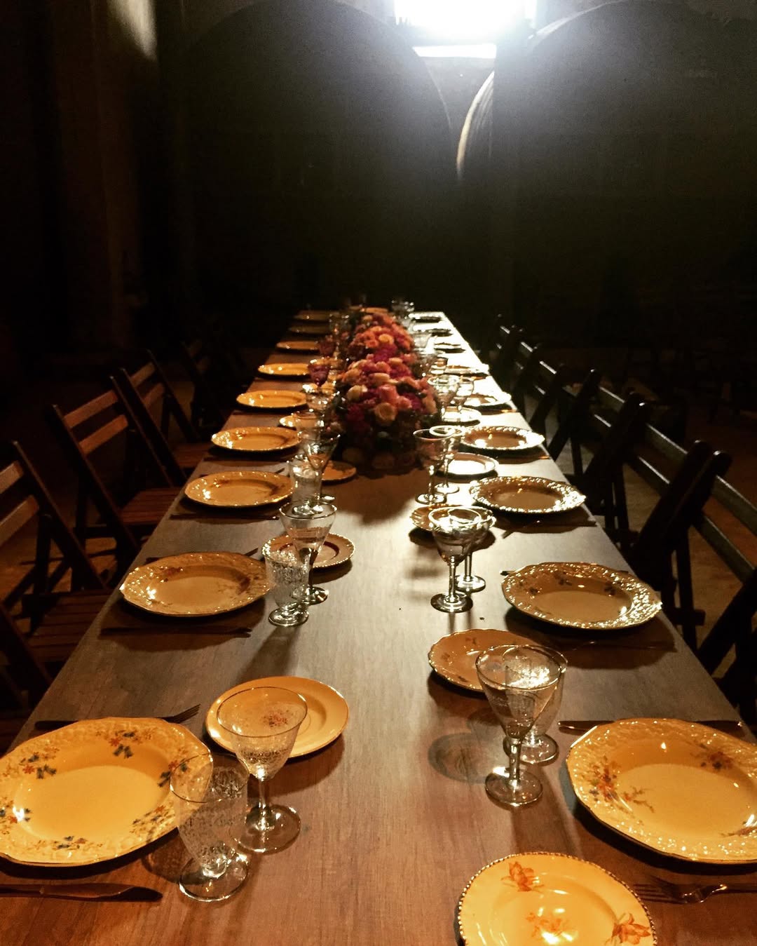 Mesa de banquete larga con platos de filo dorado y copas de cristal