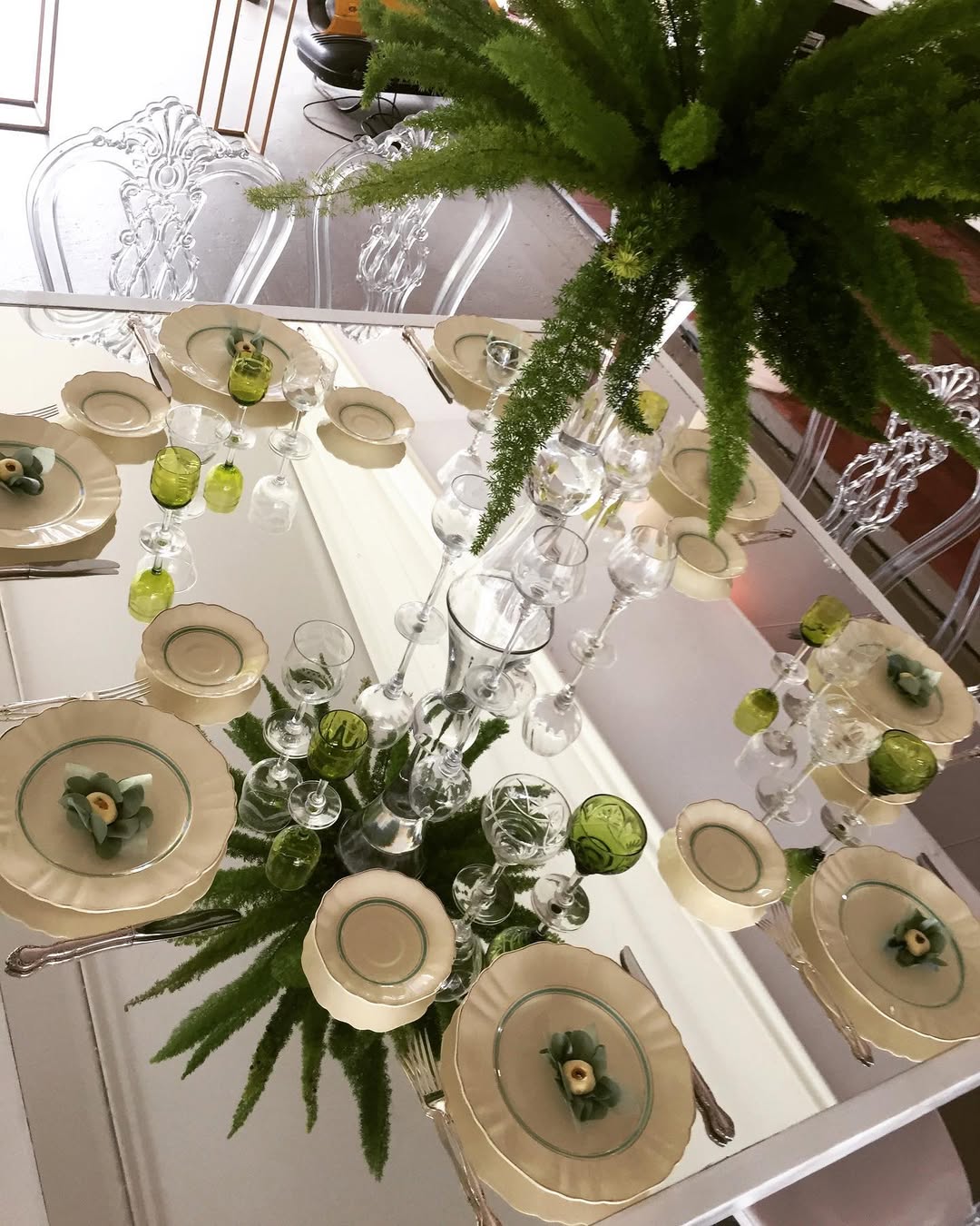 Mesa espejada con platos de filo verde, cristalería verde y helechos